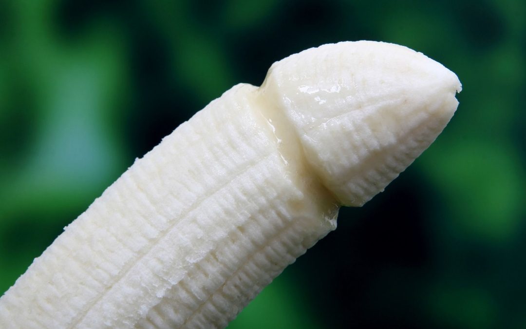 Vista parcial sobre fondo verde y negro de un plátano pelado en el que se ha dibujado un surco alrededor de la punta para que parezca un pene con el glande